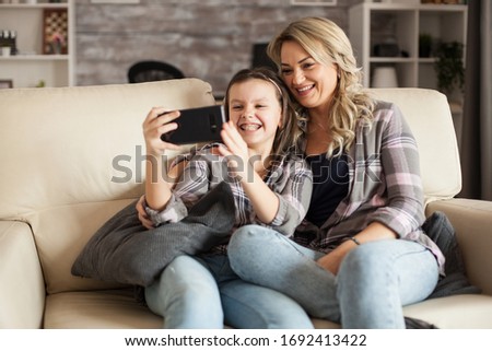 Little girl showing her braces while taking a selfie with her mother sitting on the couch in living room.