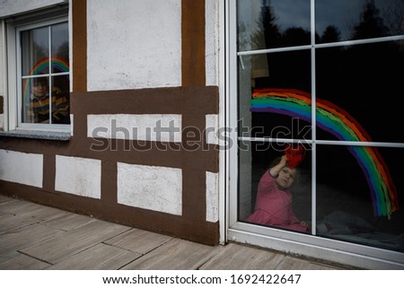 Two kids, school boy and toddler girl with rainbow painted with colorful window color during pandemic coronavirus quarantine. Children painting rainbows with the words Let's all be well