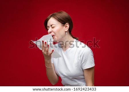 Attractive woman is sick, she coughs and sneezes, picture isolated on red background
