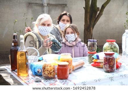 beautiful old grandmother with gray hair in a medical mask with a granddaughter and daughter in a gray shawl sits at a table on the street in the market where they sell food, alcohol and canning
