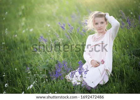 outdoor portrait of a young blond girl sitting in a blooming meadow hair in a wind