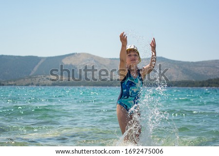 little young girl playing on a beach splashing water in a sea on summer holiday in croatia