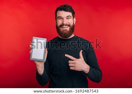 happy bearded man pointing at tablet screen over red background
