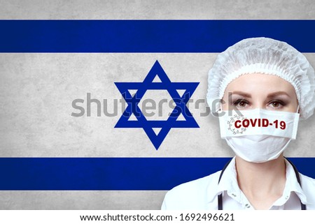 Female doctor in medical mask with the inscription COVID-19 on a blurred background of the flag of Israel. Pandemic virus COVID-19. Healthcare and medical concept. 