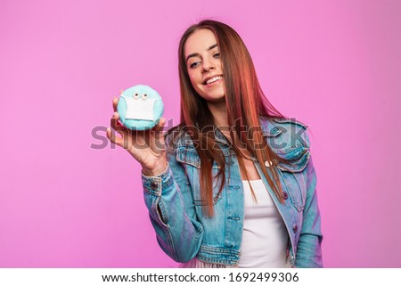 Happy pretty young woman in stylish blue denim jacket in white t-shirt with cute smile with creative donut in protective mask posing near pink wall in the studio. Modern girl model. Positive emotions.