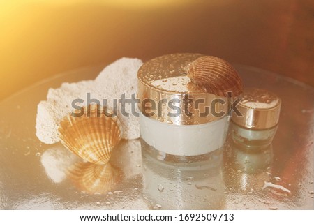 concept of skin care with marine ingredients jar of face cream and a small jar of cream under the eyes with drops of water and seashells on a dark background