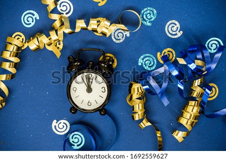 Black clock alarm clock among gold osperpantin, sequins on a blue background. Holiday content.