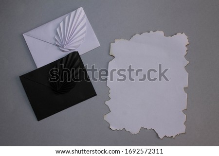 Black and white card envelope next to worn papyrus on silver background