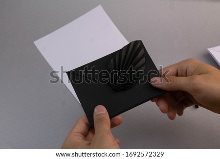 Hands holding black card envelope next to white sheet on a gray background