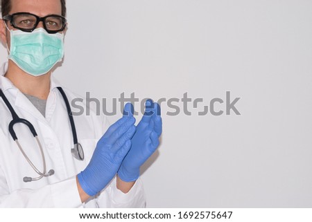 Doctor with blue gloves, mask and goggles clapping on a white background. Free space for text.