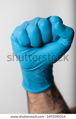 Man's hand in blue medical gloves raises his fist. Close-up view