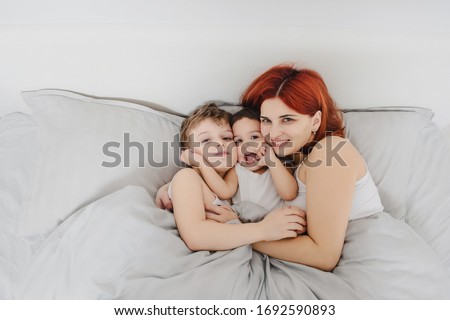 Morning family concept. Top view of mother with her children son and daughter in white t-shirts waking up, smiles, kissing, and having fun