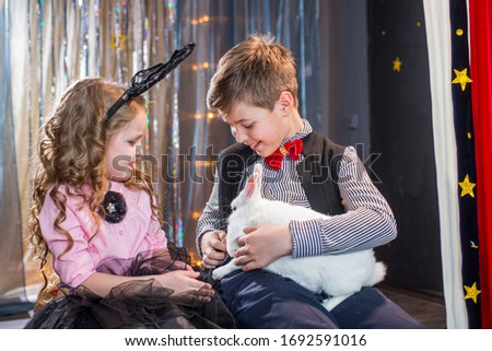A boy and a girl with a white rabbit in a hat in a circus