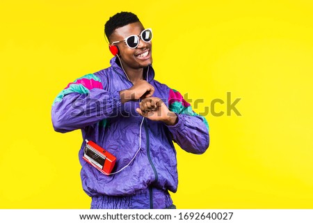 African American young man, in a jacket in the style of the 90s, with a retro cassette player, hears music, the mood of dancing and fun, yellow and purple colors Royalty-Free Stock Photo #1692640027