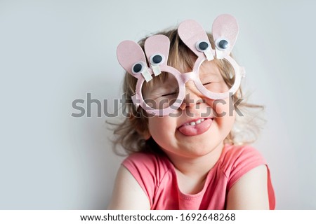 Easter Bunny. Cute happy little child girl is wearing glasses bunny ears shows language/tongue, on Easter, on white. Very  expressive emotions of joy. Emotions, expressiveness, childish spontaneity.