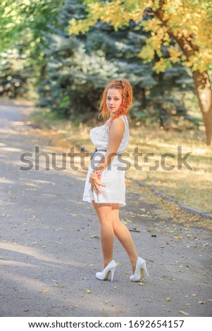 Red-haired girl in a white dress in the park in early autumn