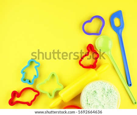 Colorful baking pans for Christmas gingerbread on a yellow background. Children's toy shovel, red penguin for making holiday cookies.