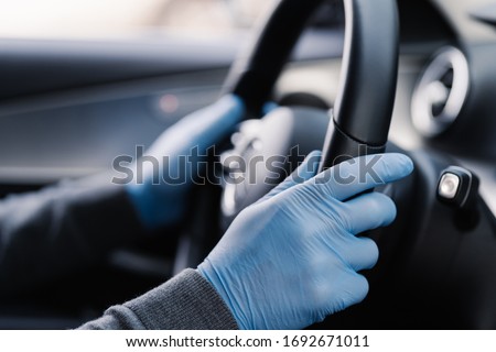 Covid-19 concept. Man drives in car, wears medical gloves, protects himself from bacteria and virus, holds car steering wheel. Coronavirus protection. Transport, quarantine and corona disease. Royalty-Free Stock Photo #1692671011