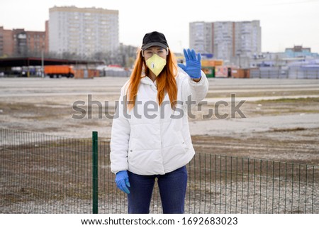 caucasian woman in a glasses, protective mask stands on the street, shows a stop sign with her hand and looks at the camera. Coronavirus, health protection, quarantine, safety and pandemic concept