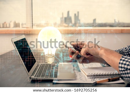 Double exposure of man's hands holding and using a digital device and bulb hologram drawing. Idea concept.
