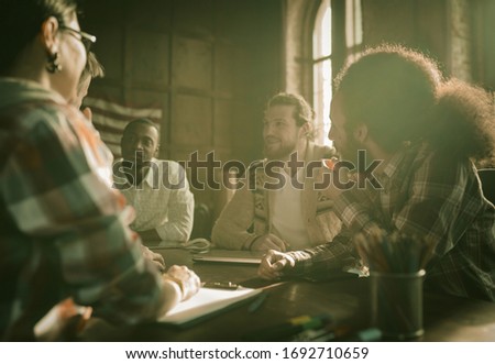 Friendly Team Of Young People Brainstorming At Business Meeting In Cozy Office Interior, Multi-Ethnic Group Of Young Smiling People chatting lively at negotiating table