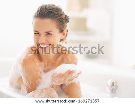 Portrait of happy young woman playing with foam in bathtub Royalty-Free Stock Photo #169271357