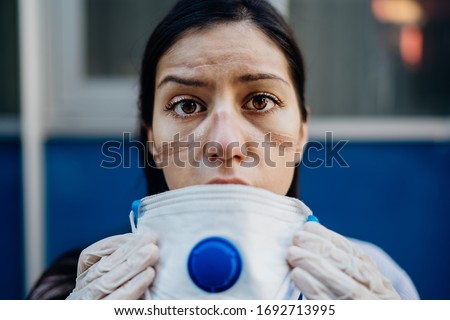 Exhausted doctor / nurse taking of coronavirus protective gear N95 mask uniform.Coronavirus Covid-19 outbrek.Mental state of medical professional.Face scars.Mask shortage.Overworked health workers Royalty-Free Stock Photo #1692713995