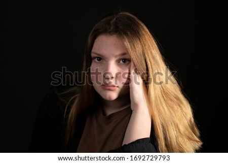 Sad teen girl on a black background with head in hands.