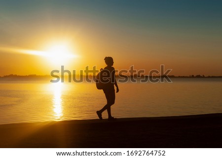 
woman in a sunset walking and taking photos with her cell phone with a beautiful sunset over the pier