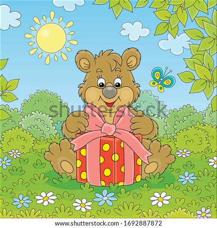 Friendly smiling little brown bear cub holding a beautiful box with a holiday gift on green grass of a pretty forest glade on a sunny summer day, vector cartoon illustration