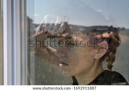 Young girl looks through the window on a sunny day	
