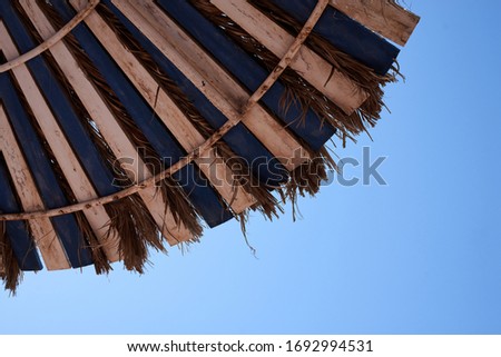 A part of blue and white wooden beach umbrella with straw on the bright light blue sky. Tropical resort background.