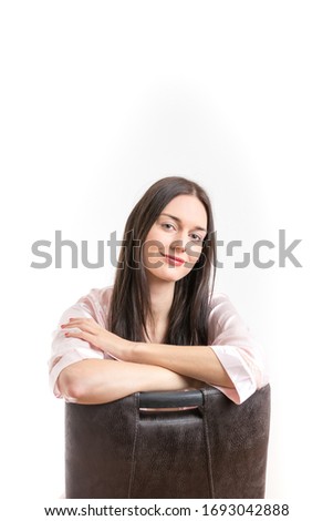 Attractive young brunette woman wearing a pink nightgown, sitting on chair with crossed arms smiling. Royalty free stock photo.