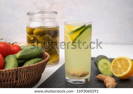 side view of lemon and lime juice with basket of tomato and cucumber on white background