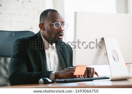 Typing text. African-american entrepreneur, businessman working concentrated in office. Looks serios and busy, wearing classic suit, jacket. Concept of work, finance, business, success, leadership.