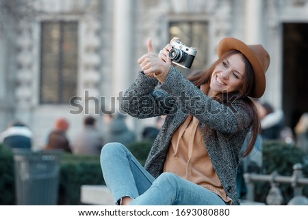 Young beautiful girl sits on a bench with a camera and shows a super gesture with her hand.