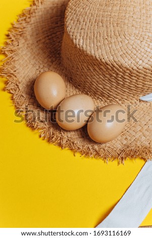 Three eggs on a yellow background with a straw hat. Happy easter. Eco-friendly farm food from the village. Chicken eggs and straw.