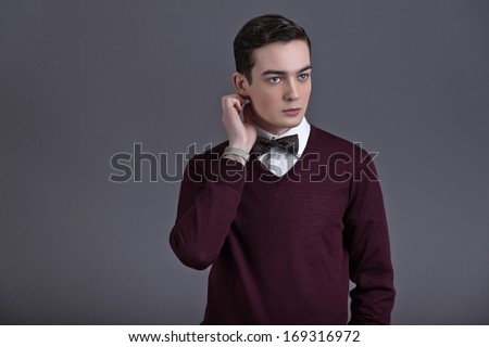 Retro fifties english style fashion young man. Wearing dark red shirt and bow tie. Studio shot against grey.