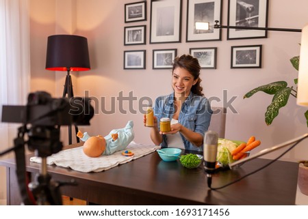 Female vlogger filming video about introducing soft food to baby nutrition and preparation of fresh fruit and vegetable porridges as part of online prenatal classes course