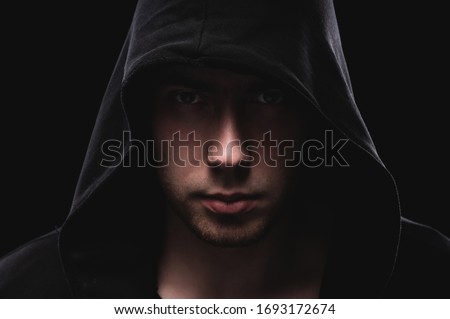 Close-up portrait of a courageous man in a deep dark hood on a black background. The concept of secrecy of secrets and people hiding from the government. Hackers and thieves. Low key