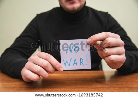 A man holding piece of paper showing word "No war". Close up
