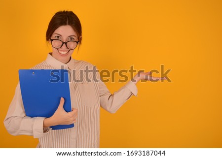 successful business woman in glasses with a blue folder on her hand holds a copy space on a yellow background