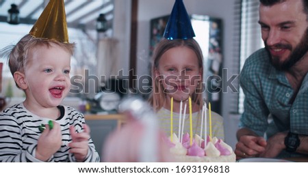 Happy young European teenage girl child blowing on birthday cake, celebrating party at home with family slow motion.