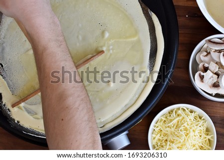 Picture from above - one person spreads the dough on a crêpe iron A man prepares delicious, homemade, sweet crepe and spreads the dough on the iron in front of a wooden background