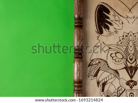 A part of wooden picture with the image of a wolf made using the technique of pyrography and decorated with a carved frame. On green background with place for text