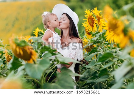 Happy mother in hat with the daughter in the field with sunflowers. mom and baby girl having fun outdoors. family concept. mom kisses her daughter. selective focus