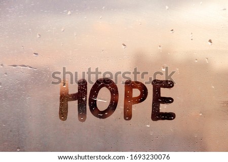 Foggy glass on window with written finger word yellow color Hope concept photo with copy space on blue and warm background