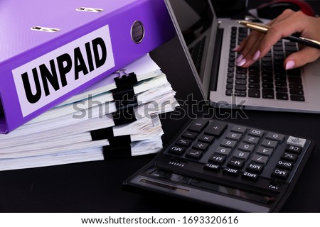 Text, word Unpaid is written on a folder lying on documents on an office desk with a laptop and a calculator. Business concept. Royalty-Free Stock Photo #1693320616