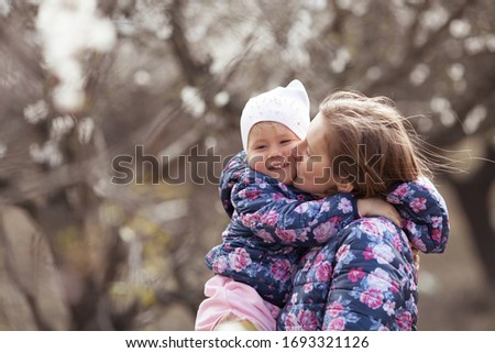 Portrait of happy mother and daughter on a background of almond trees in blossom, a woman and a child walk in the spring garden, outdoor