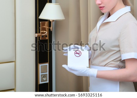 A white-gloved maid holds a sign that reminds her to stop Smoking. Photo in the hotel interior. Caring for residents. Copy space.